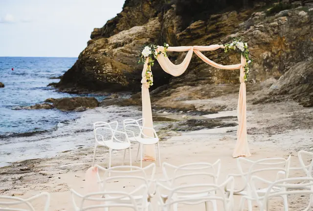 El arco de tul de la ceremonia y las sillas blancas en una cala junto al mar