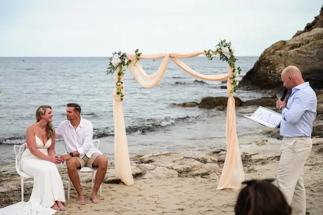 Los novios sentados frente al oficiante durante la ceremonia en la playa