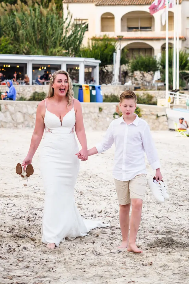 La novia llega por la playa de la mano de un niño, con las sandalias en la mano