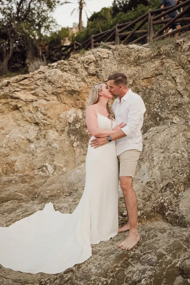 Los novios se besan sobre las rocas con la cola del vestido extendida