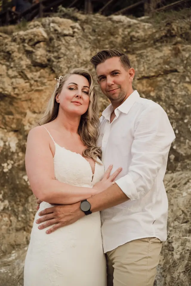 Retrato de los novios abrazados frente a las rocas de la cala