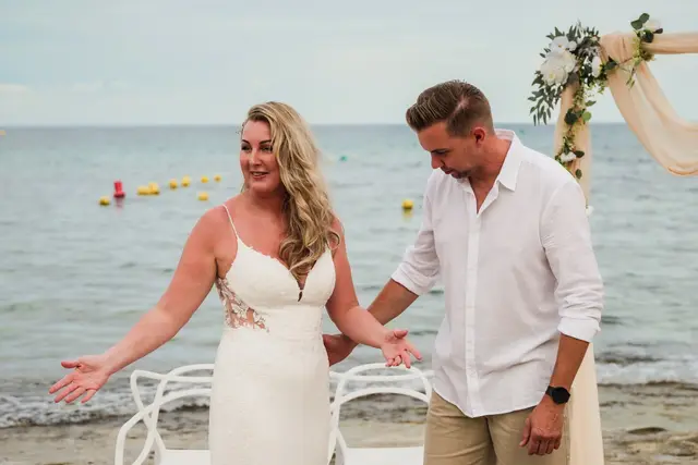 Los novios se ríen delante del arco, frente al mar