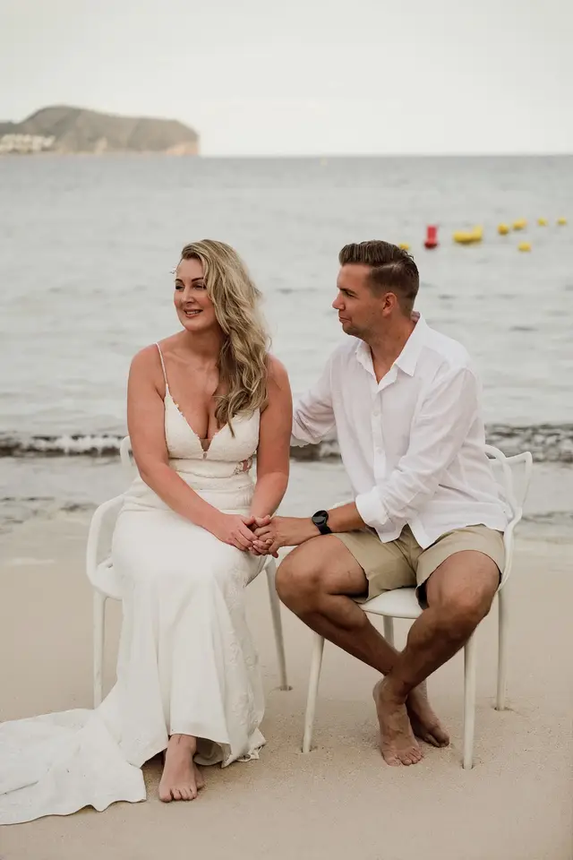 Los novios sentados de la mano durante la ceremonia, con el mar detrás